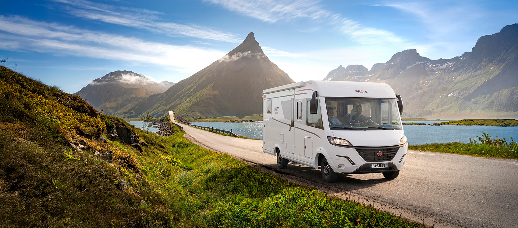 Vue d'un camping-car intégral roulant sur une route rectiligne, un lac et des montagnes